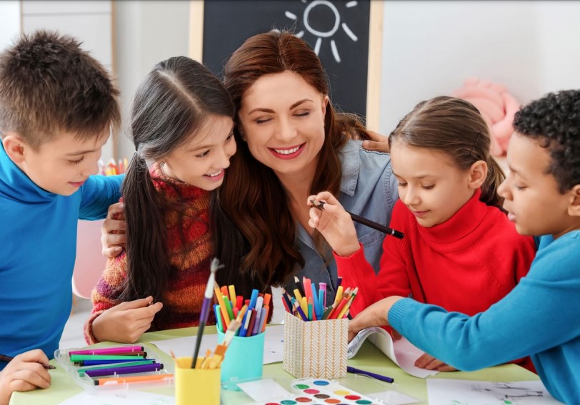 Profesora junto a tres estudiantes sonriendo y pintando con lápices de colores